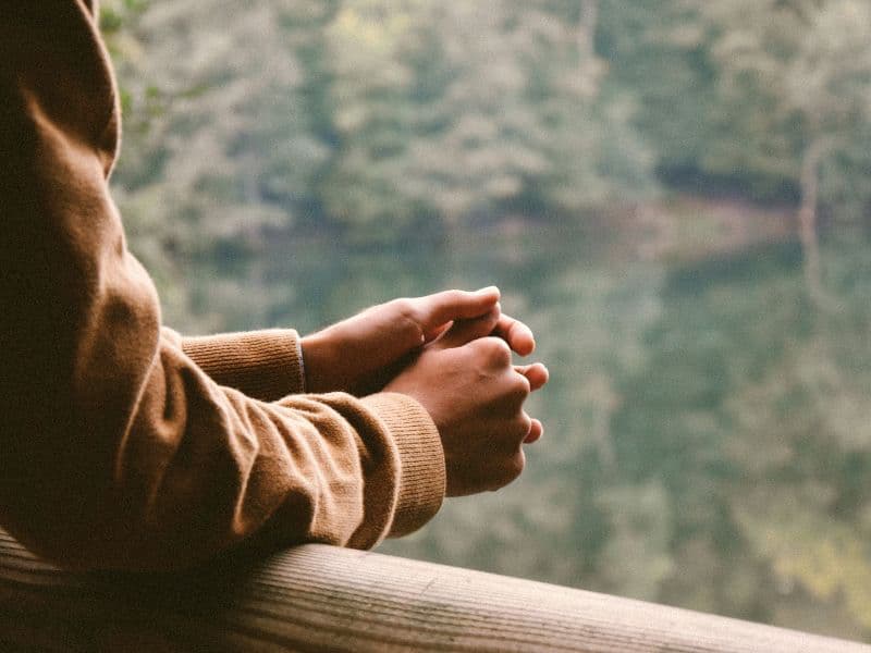 Person clasping hands overlooking the river.