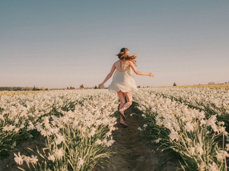 Woman running through daffodils representing hope and new beginnings as she closes the last page of a heavy chapter.