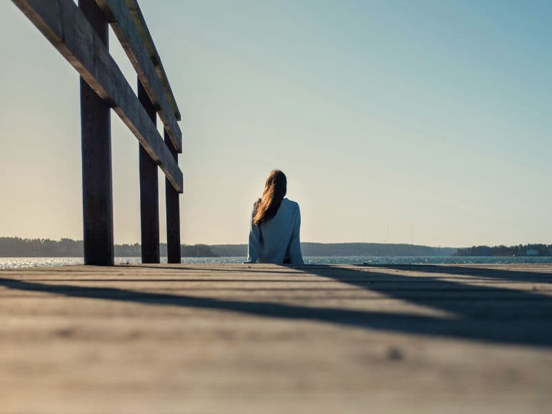 Person reflecting by the dock at sunrise reflecting hope and healing.
