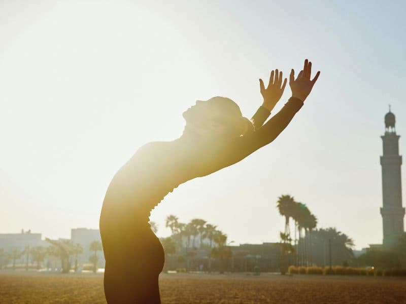 Woman stretching in the sun representing healing and the feeling of being free.
