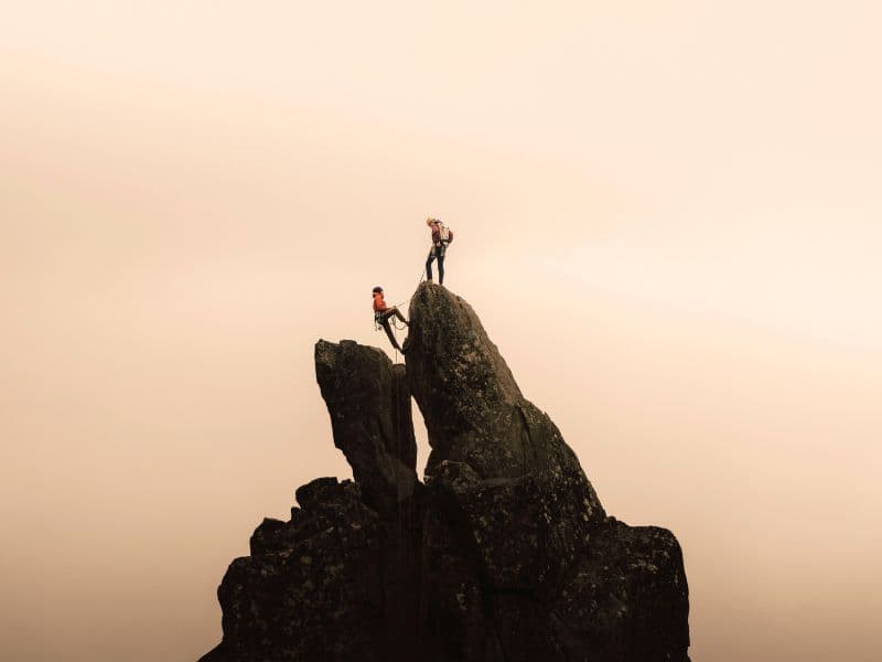 Person trusting a loved one to support them on their climb to the top of the mountain.