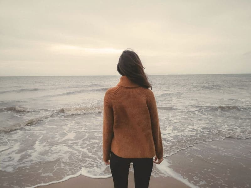 Woman looking deeply at a large body of water, representing the vast ways that childhood trauma can impact a person as an adult.