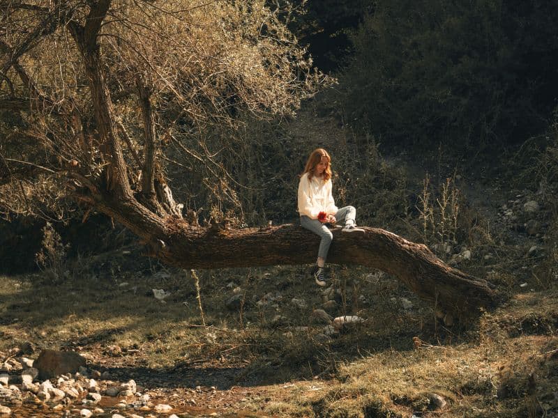 Woman sitting alone on a tree, reflecting quietly.
