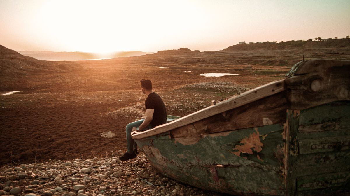 Boy sitting on an abandoned ship staring at the sunset, representing the abandoned feeling children are left with after emotional neglect.