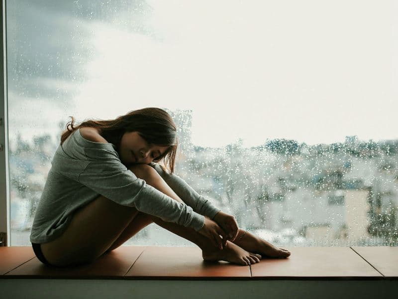 Girl sitting down hugging her legs, appearing withdrawn and emotionally distracted.
