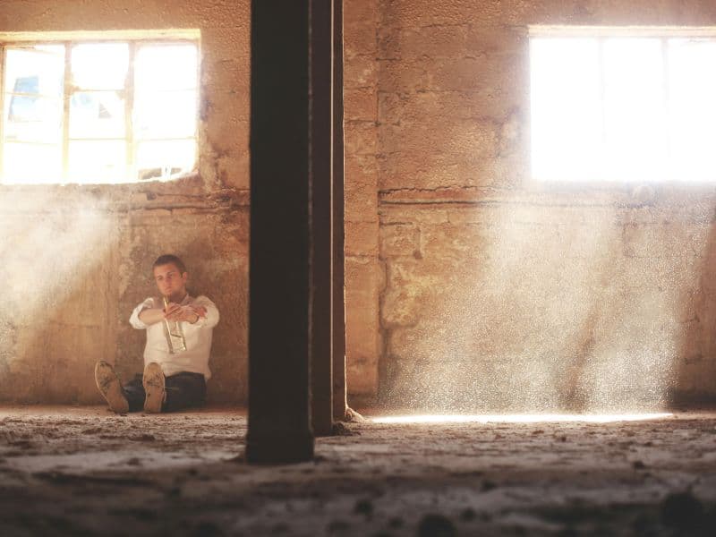 Man sitting alone on the floor in deep thought, seeming to feel helpless and overwhelmed.