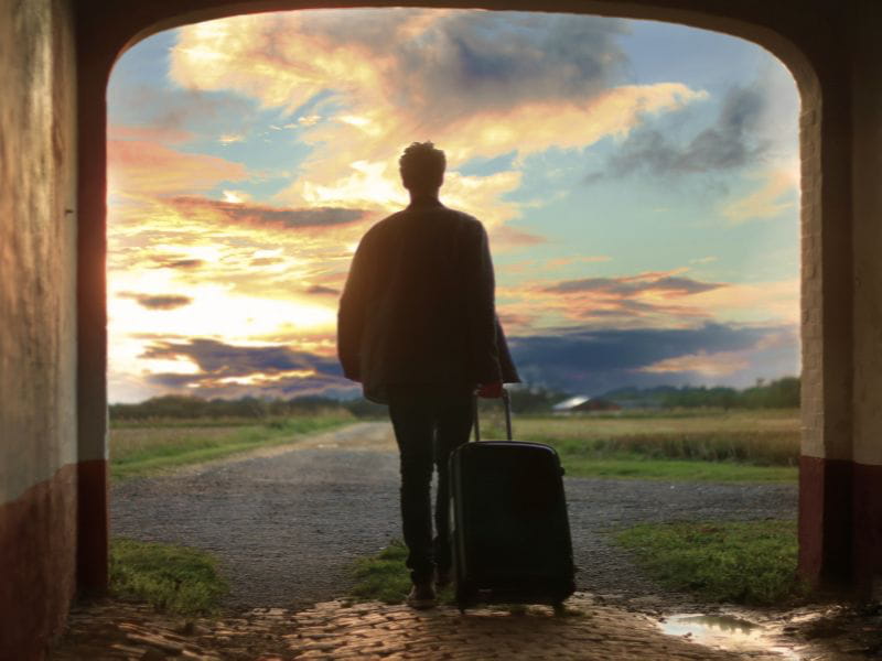 Man walking away with suitcase towards the sunset representing leaving after abuse.