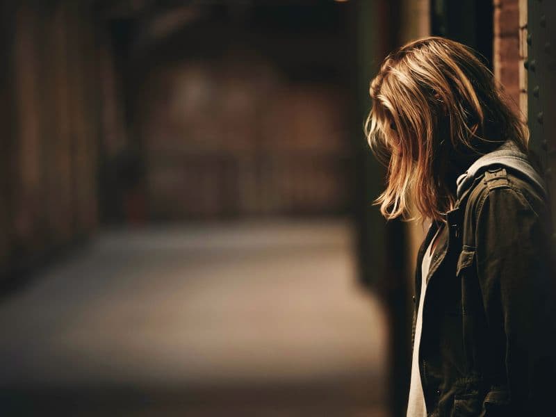 Woman leaning on wall looking down, appearing to be stressed.
