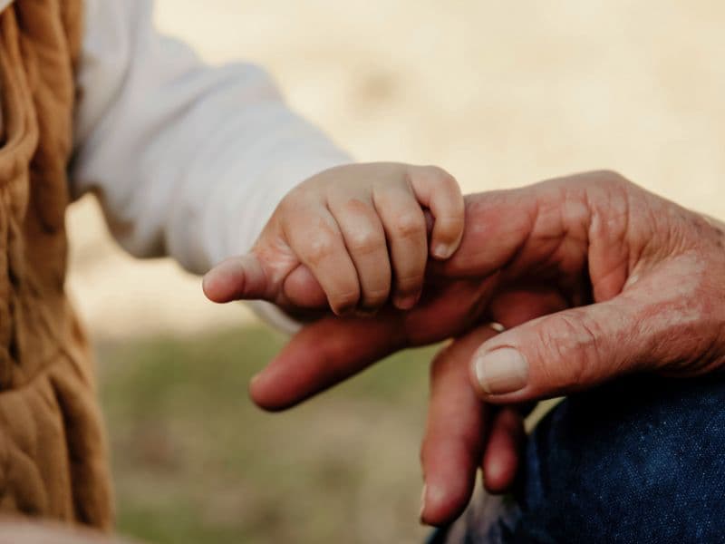 Child holding an adult’s finger, representing early emotional bonds, attachment, and how childhood experiences shape adult relationships.