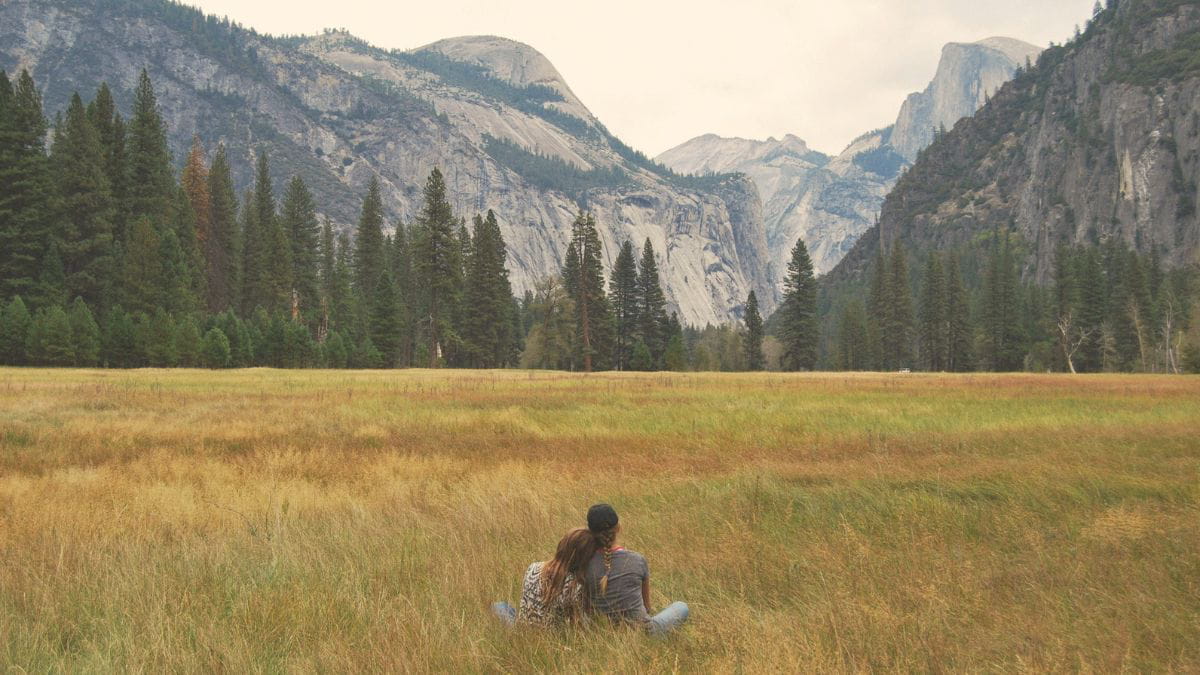 Two people sitting closely together in a field overlooking mountains, symbolizing emotional connection, healing, and the impact of childhood trauma on adult relationships.
