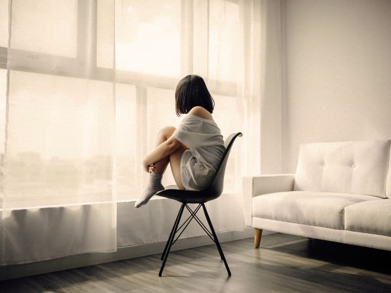Woman looking outside through a closed curtain representing the barriers that make it difficult to identify abuse.