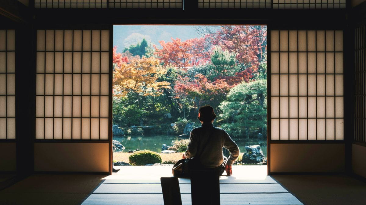 Man sitting inside a temple looking out at colourful trees, reflecting on mental health and cultural expectations in South Asian families.