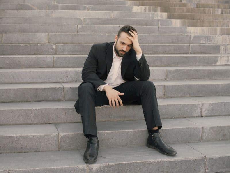 Businessman sitting on stairs in distress, representing burnout and emotional exhaustion caused by hidden trauma.