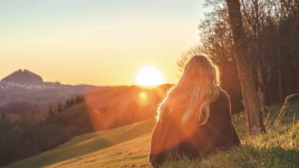 Woman sitting in the grass watching the sunrise as a symbol of healing without therapy and emotional recovery.