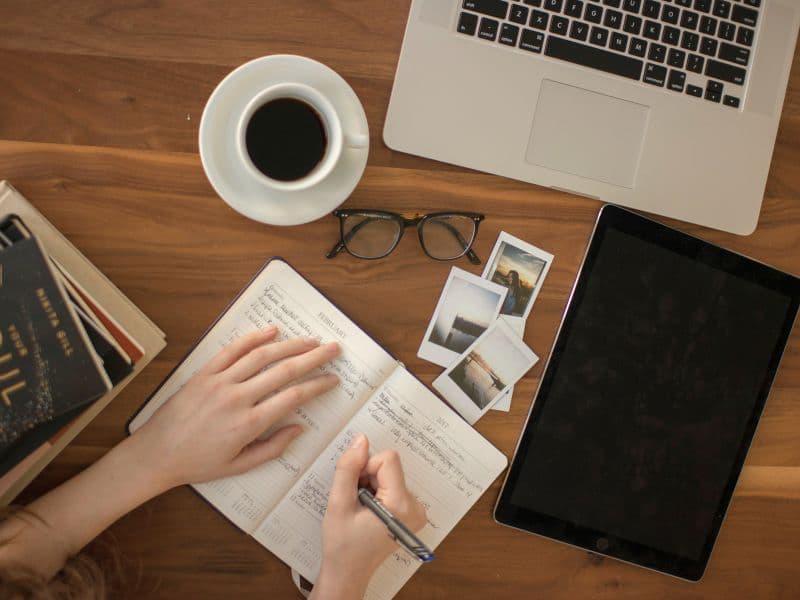 Person writing in a journal with books and coffee while practicing self-reflection for emotional healing without therapy.