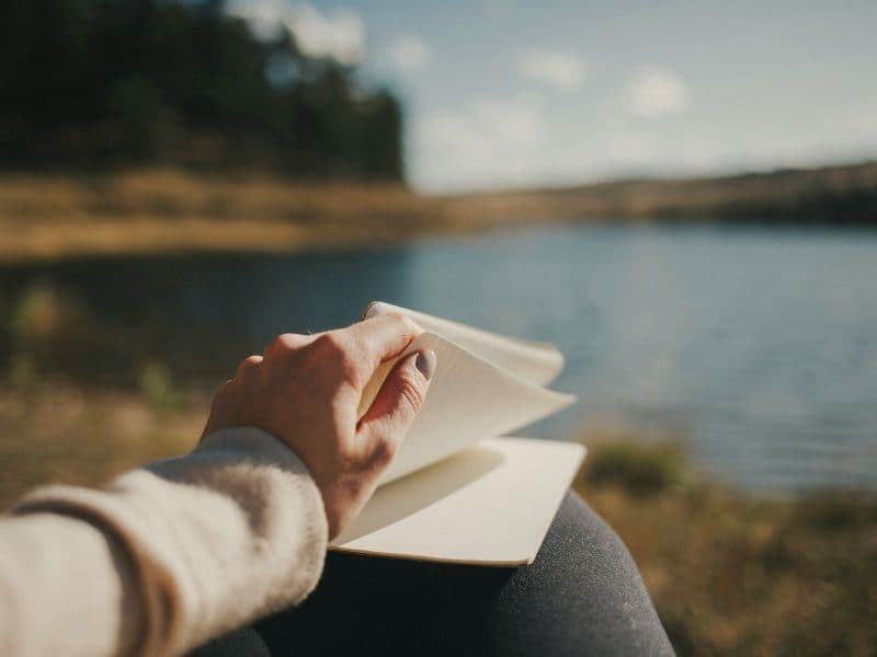 Person flipping through a notebook in nature to reflect on healthy emotional healing strategies.