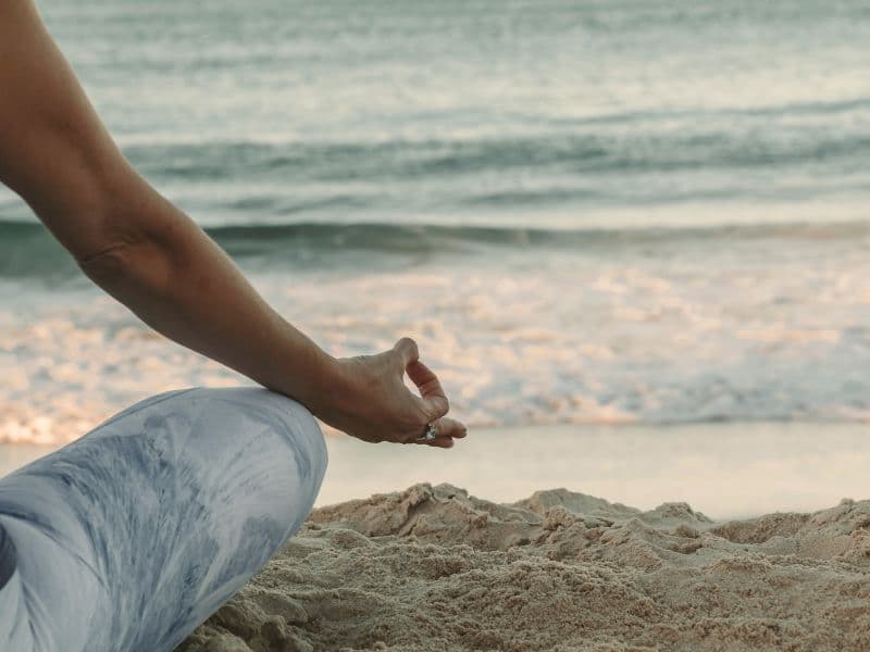 Person meditating on the beach to support nervous system regulation and emotional healing without therapy.
