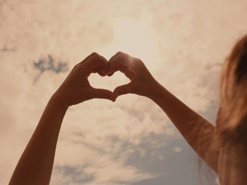 Hands forming a heart shape against the sky to represent self-compassion during the healing journey.