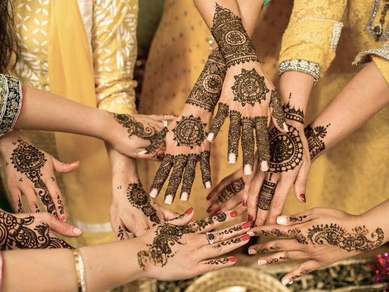 Hands of South Asian women decorated with henna gathered together, symbolizing family bonds, community, and cultural expectations.