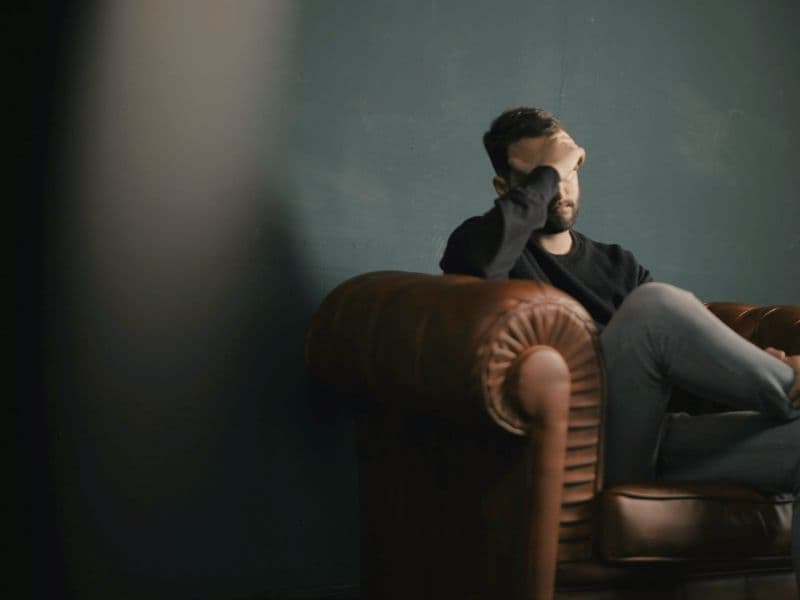 Man sitting on a couch with his hand on his head, reflecting the emotional pain of grieving what cannot be changed.