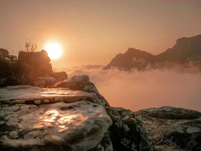 Rocky mountain landscape at sunset with low clouds, symbolizing carrying both healing and grief while moving forward.