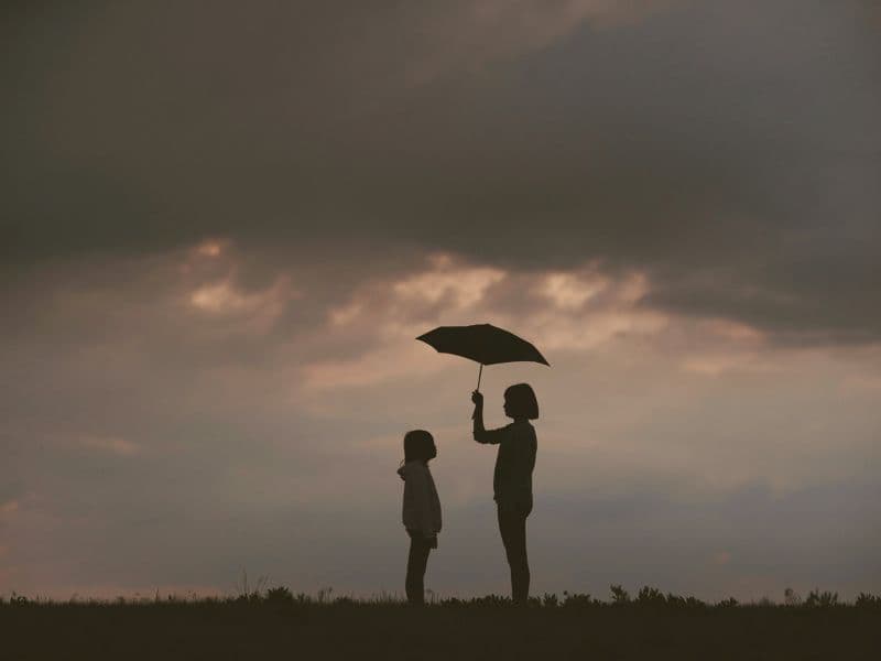 Older person holding an umbrella over a child in nature, symbolizing compassion for your younger self while healing from childhood trauma.