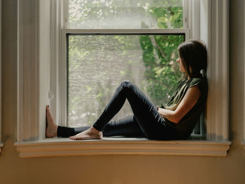 Woman sitting by a window in quiet reflection after recognizing the impact of childhood abuse.