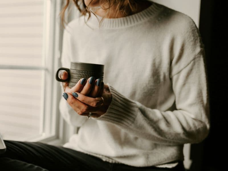 Woman holding a warm cup with both hands in a quiet moment of reflection.