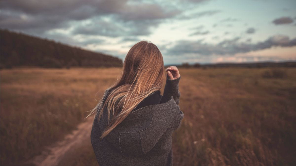 Woman standing in an open field looking into the distance, reflecting on past experiences of abuse.