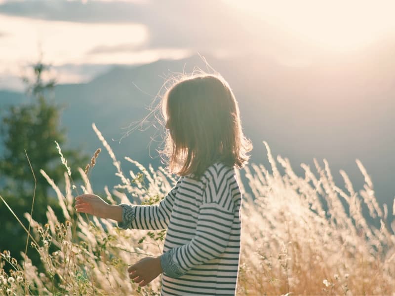 Child touching tall wild grass while walking through nature.