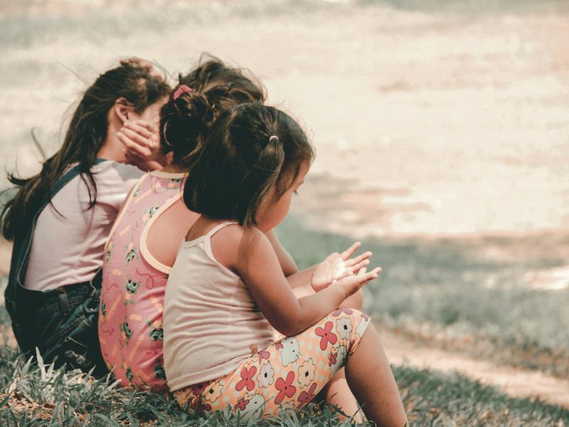 Three young girls sitting together on the grass, representing the childhood moments and connections that some trauma survivors grieve.