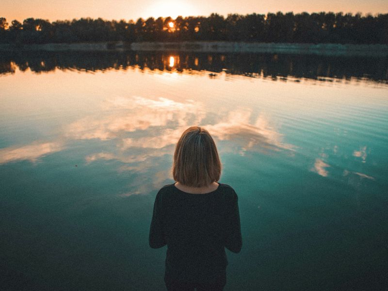 Woman looking out over calm water at sunset while reflecting on grief and healing from childhood trauma.