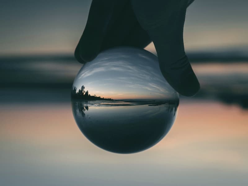 Ocean and trees reflected clearly inside a glass ball with nature blurred in the background.