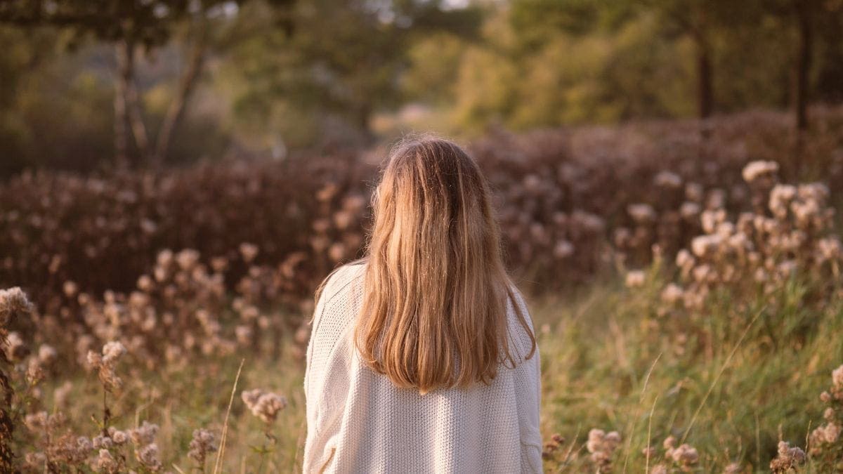 Woman standing in nature looking at flowers and trees.