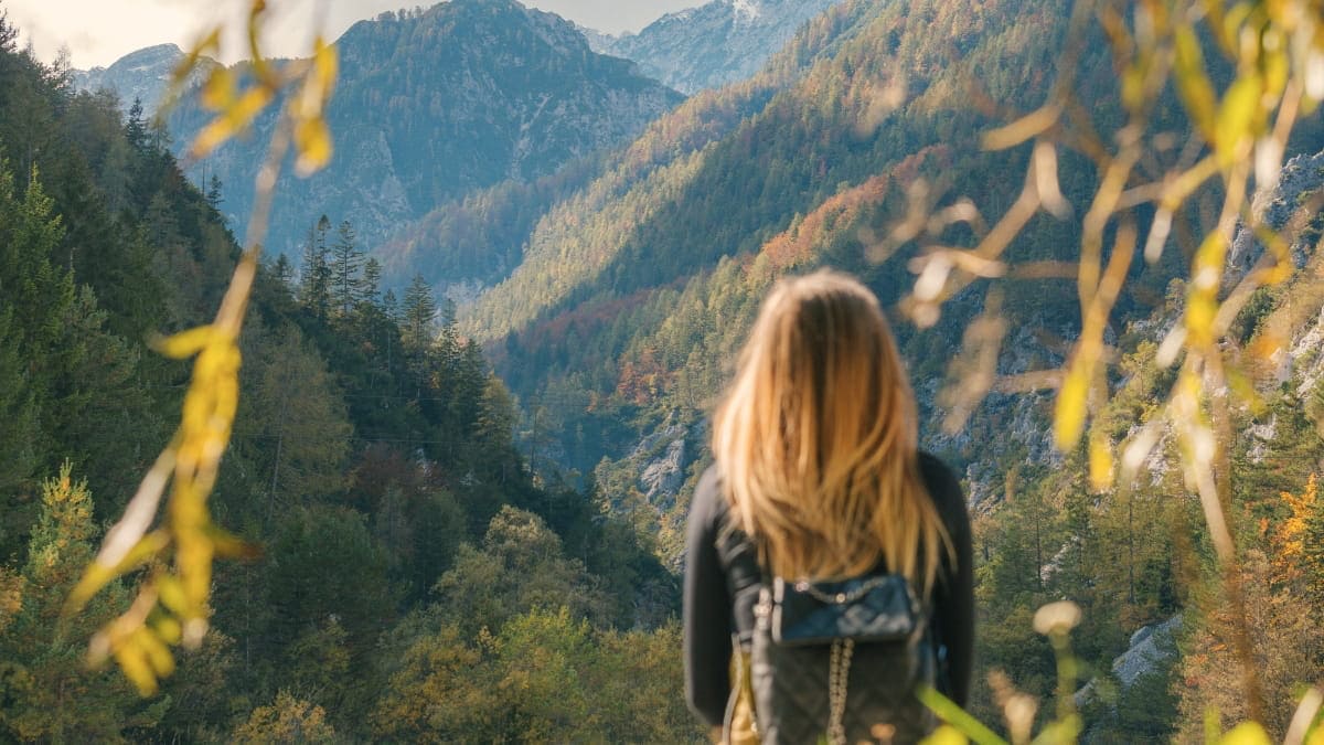 Woman with a backpack standing in the mountains and looking toward the distant peaks.