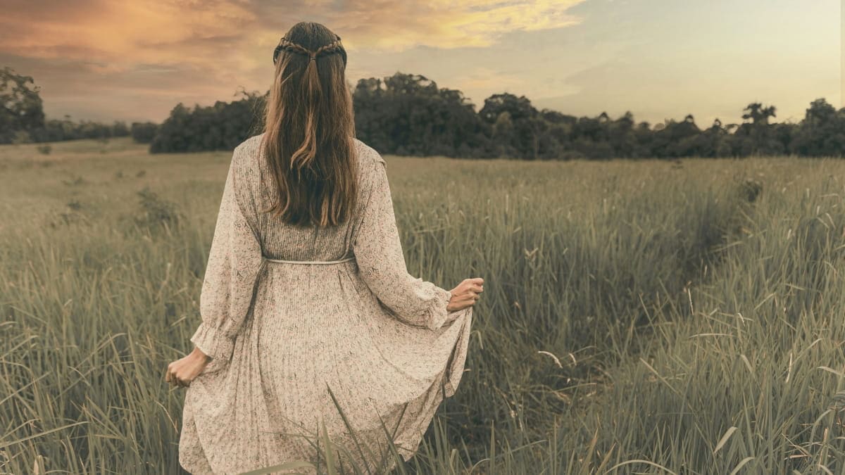 Woman in a prairie dress standing in a field and looking into the distance.