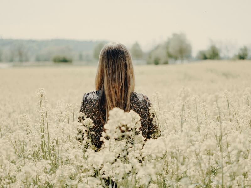 Woman standing among tall flowers and looking across a field.